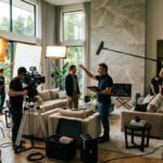 Scène de tournage dans un salon moderne et lumineux, avec équipe technique, acteur, caméra et matériel professionnel.
