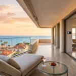 Balcon de luxe à Cannes avec transat et boisson, donnant sur la Méditerranée, les palmiers et la ville au coucher du soleil.
