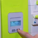 Gros plan sur une main interagissant avec un compteur Linky affichant l'injection solaire. Panneaux solaires visibles sur le toit en arrière-plan.