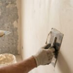 Un artisan applique un enduit à la chaux sur un mur avec une lisseuse en acier.
