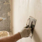 Un artisan applique un enduit à la chaux sur un mur avec une lisseuse en acier.