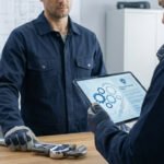 Deux plombiers en discussion, l'un montrant les termes d'une police d'assurance décennale sur une tablette, près d'une clé à molette.