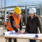 Un ingénieur et une architecte en casque de chantier étudient des plans sur un site de construction en plein air.