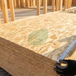 Gros plan sur une pile de panneaux OSB 18mm BuildTech Pro sur un chantier. Un ouvrier mesure avec un ruban, un logo feuille est visible.